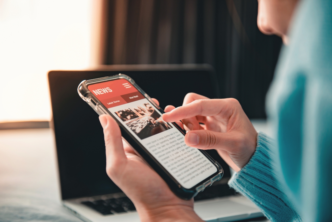 Online news on a smartphone. (Mockup website). Woman reading news or articles in a mobile phone screen application at home. Newspaper and portal on internet.